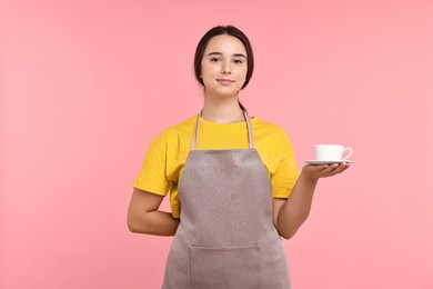 Photo of Girl in apron with cup of coffee on pink background. Work for teenagers