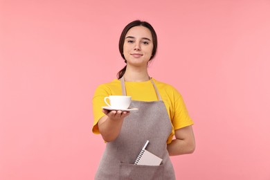 Photo of Girl in apron with cup of coffee on pink background. Work for teenagers