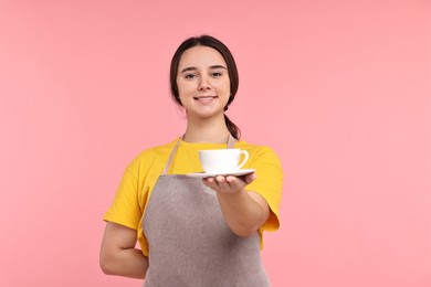 Photo of Girl in apron with cup of coffee on pink background. Work for teenagers