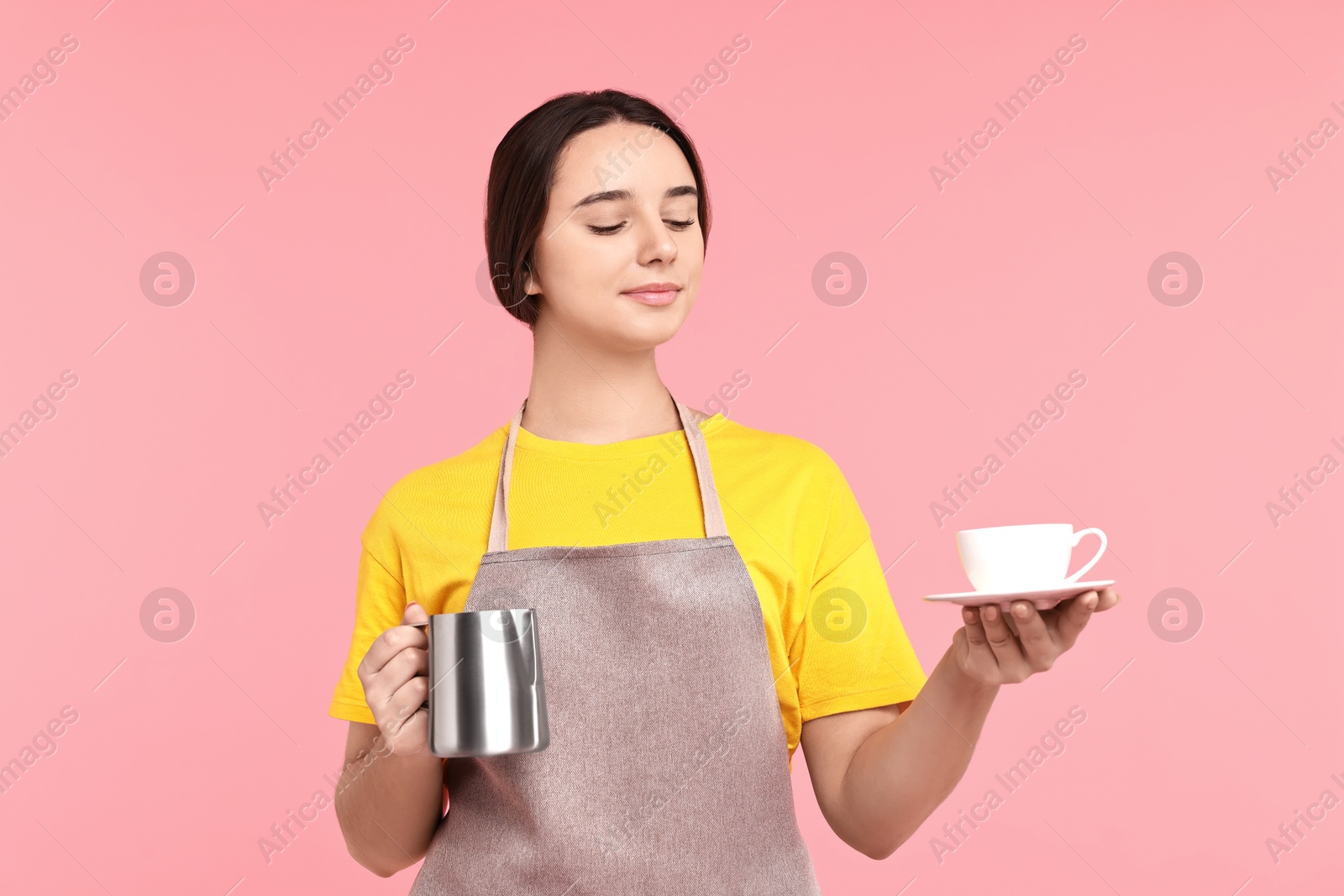 Photo of Girl in apron with pitcher and cup of coffee on pink background. Work for teenagers