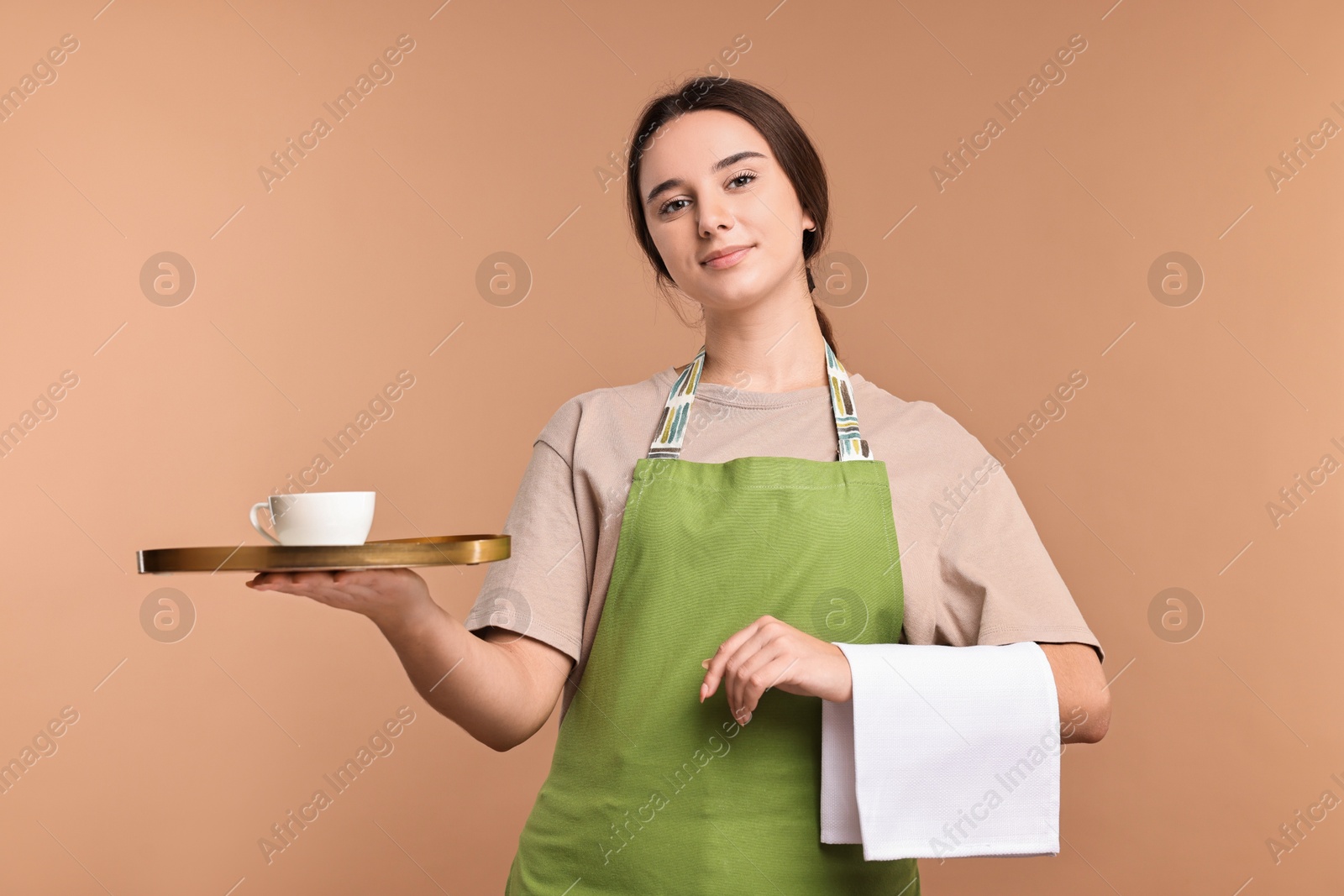 Photo of Girl in apron with cup of coffee on pale brown background. Work for teenagers