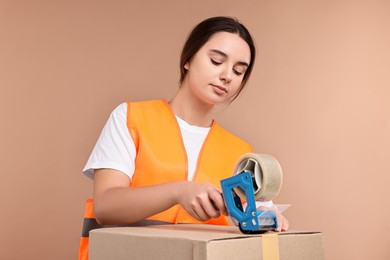 Photo of Girl packing box with adhesive tape on pale brown background. Work for teenagers