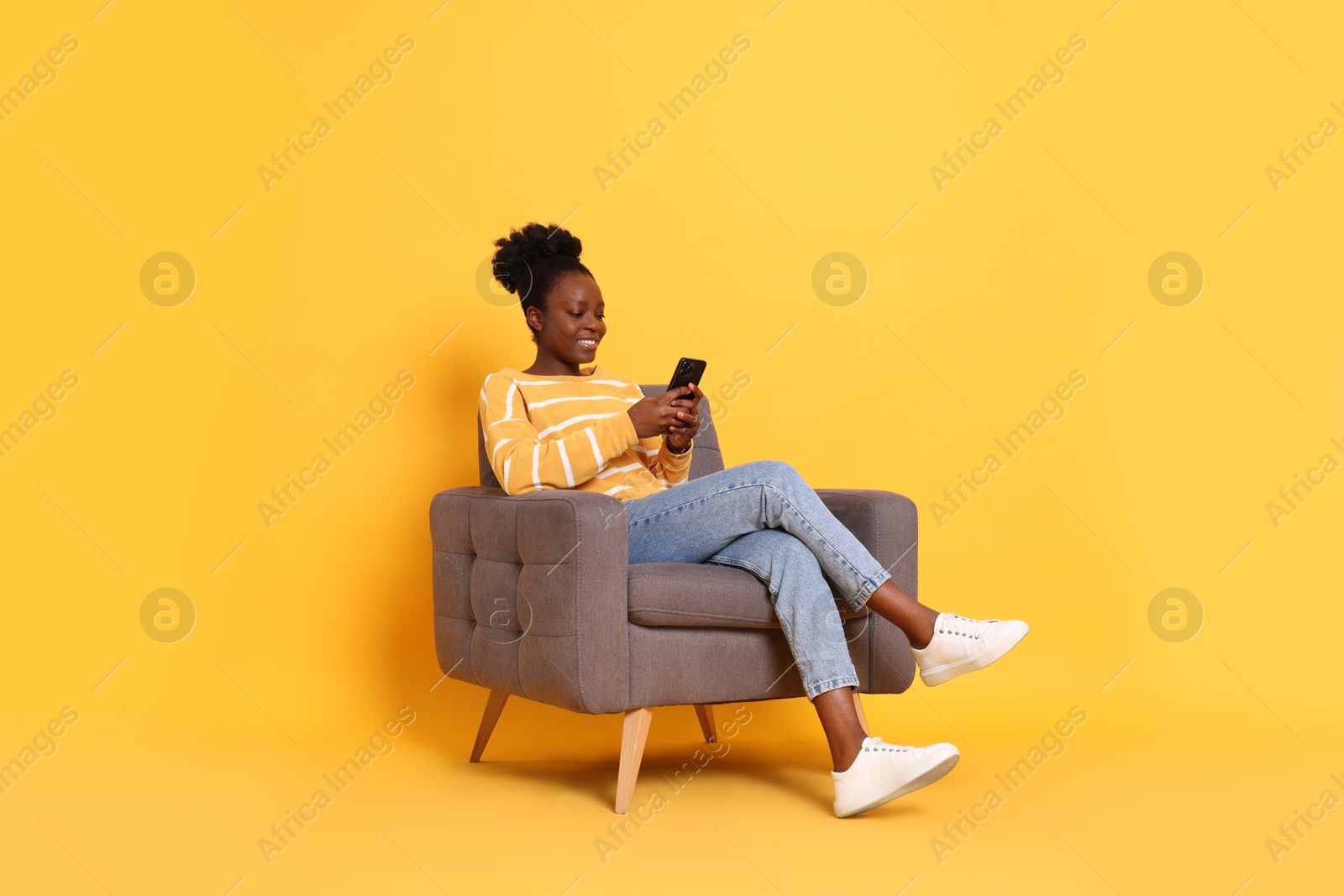 Photo of Smiling woman with smartphone sitting in armchair on yellow background