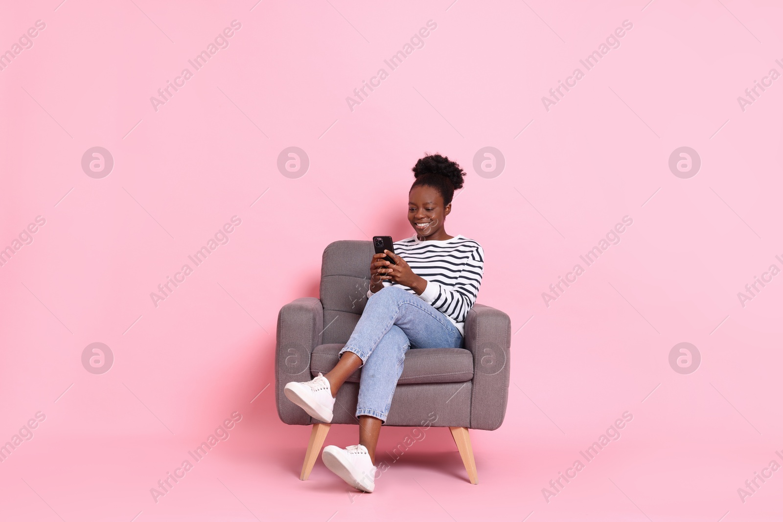 Photo of Smiling woman with smartphone sitting in armchair on pink background