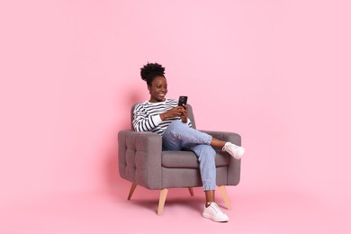 Photo of Smiling woman with smartphone sitting in armchair on pink background