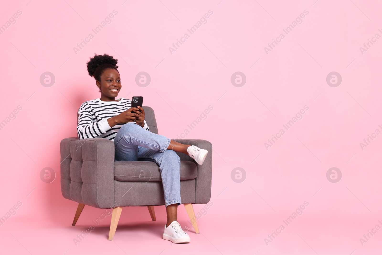 Photo of Smiling woman with smartphone sitting in armchair on pink background. Space for text