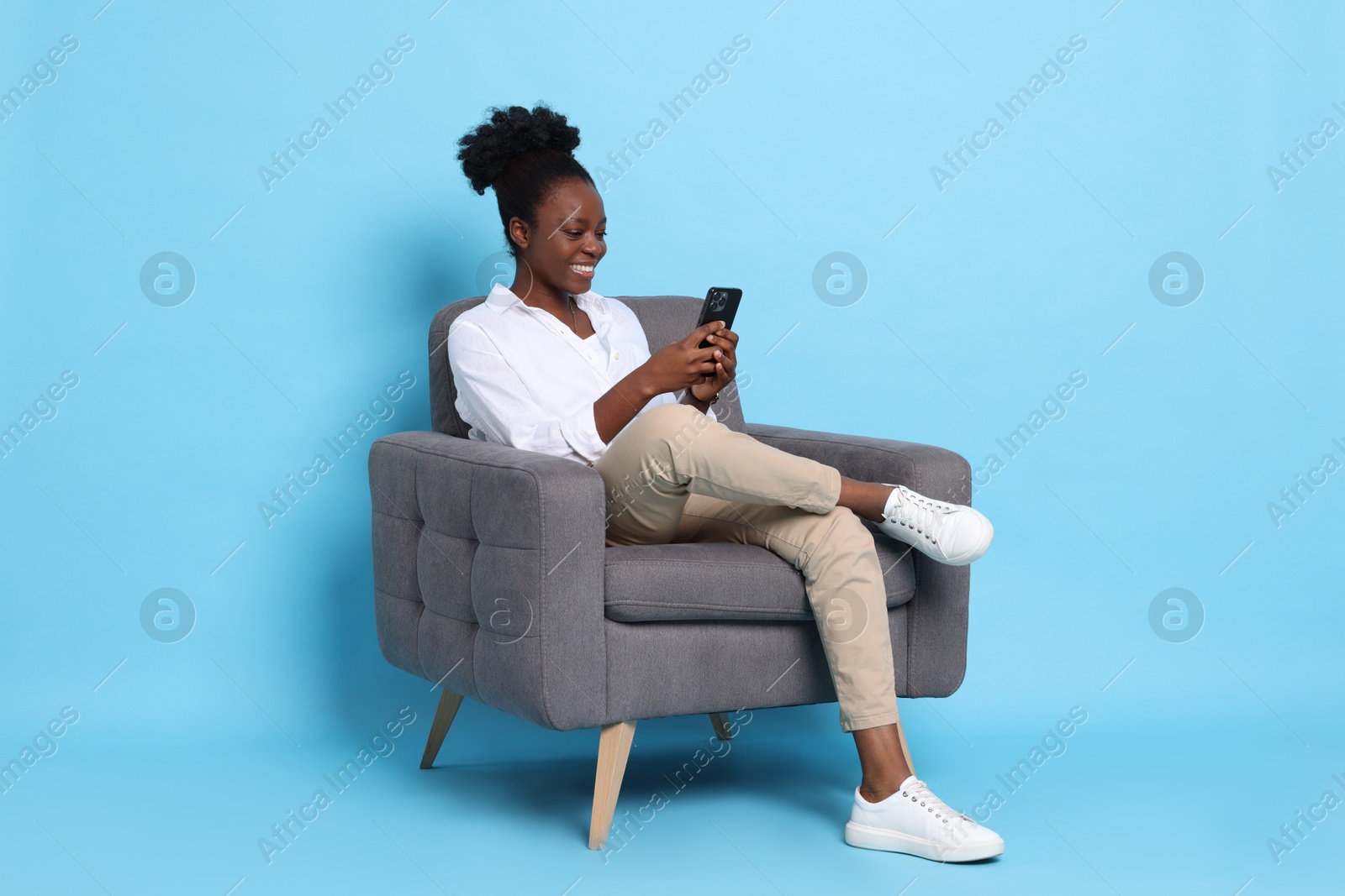 Photo of Smiling woman with smartphone sitting in armchair on light blue background