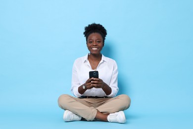 Photo of Happy woman with smartphone on light blue background