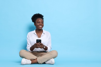 Photo of Happy woman with smartphone on light blue background. Space for text