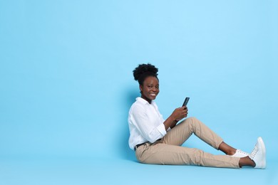 Photo of Happy woman with smartphone on light blue background. Space for text