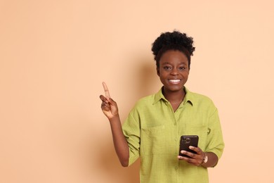 Photo of Cheerful woman with smartphone pointing at something on beige background. Space for text