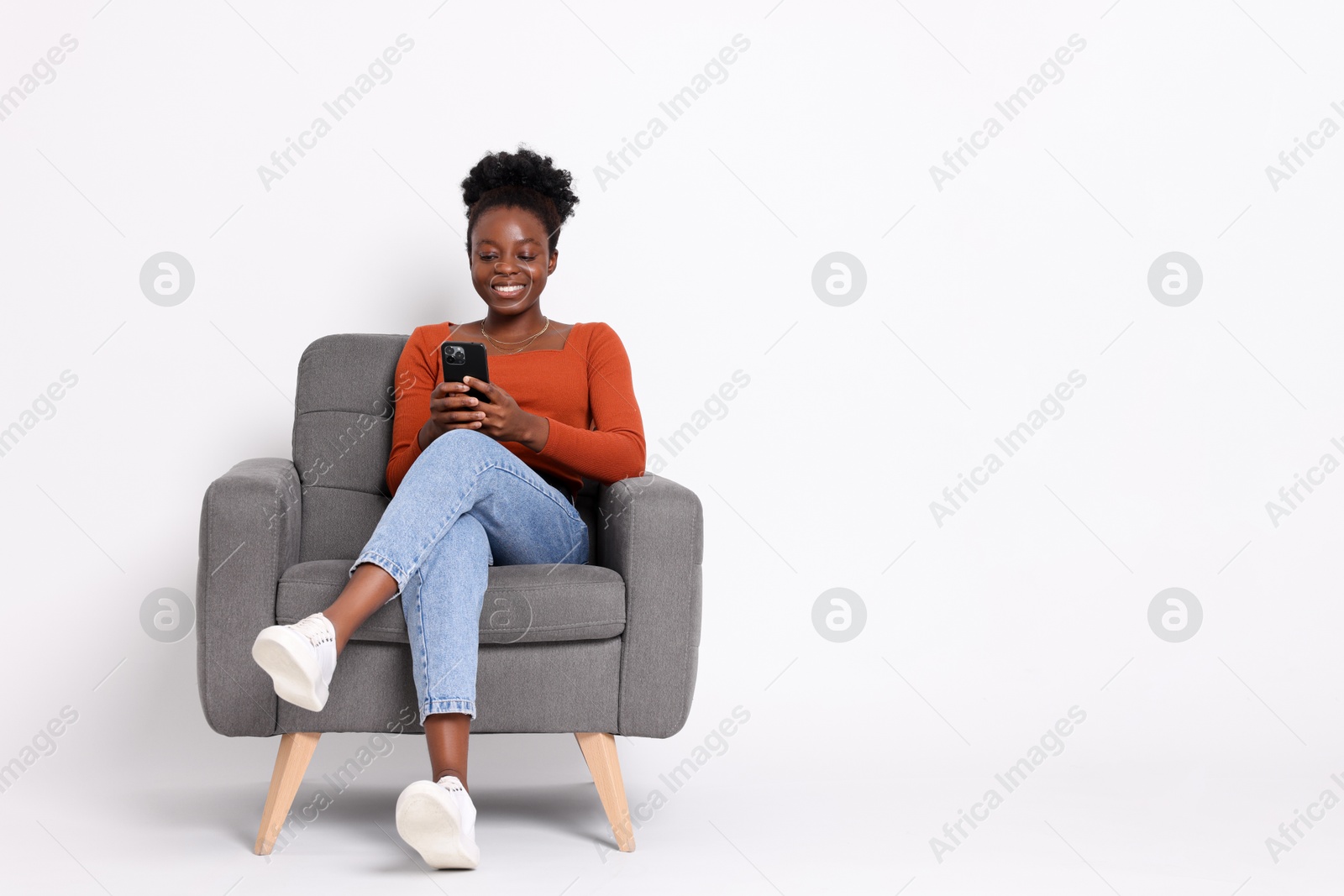 Photo of Smiling woman with smartphone sitting in armchair on white background. Space for text