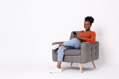 Photo of Smiling woman with smartphone sitting in armchair on white background. Space for text