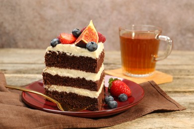 Photo of Piece of delicious chocolate sponge cake with berries and tea on wooden table, closeup