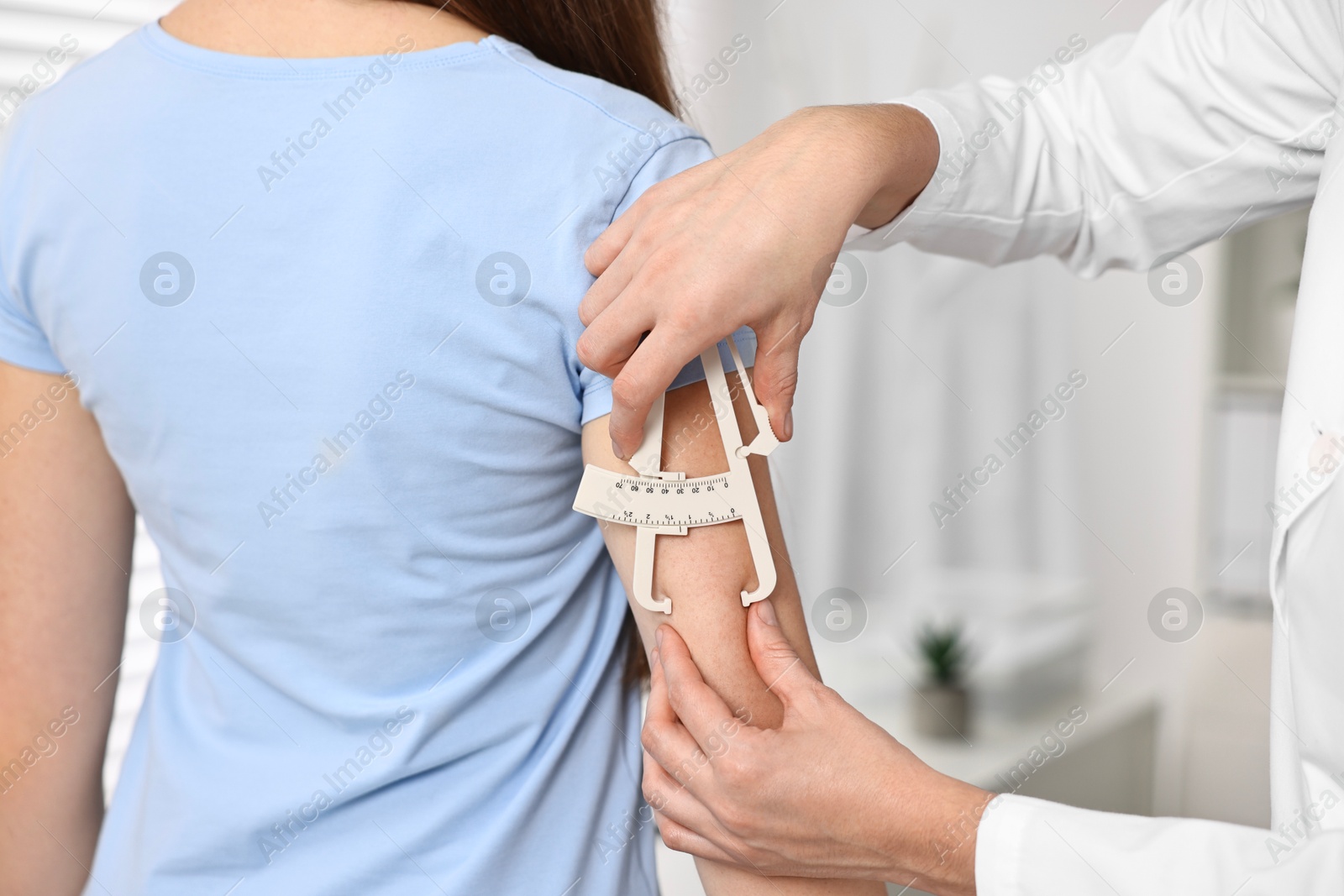 Photo of Doctor measuring woman's body fat with caliper in clinic, closeup