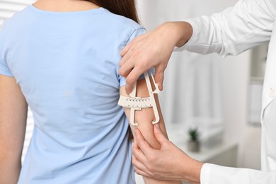 Photo of Doctor measuring woman's body fat with caliper in clinic, closeup