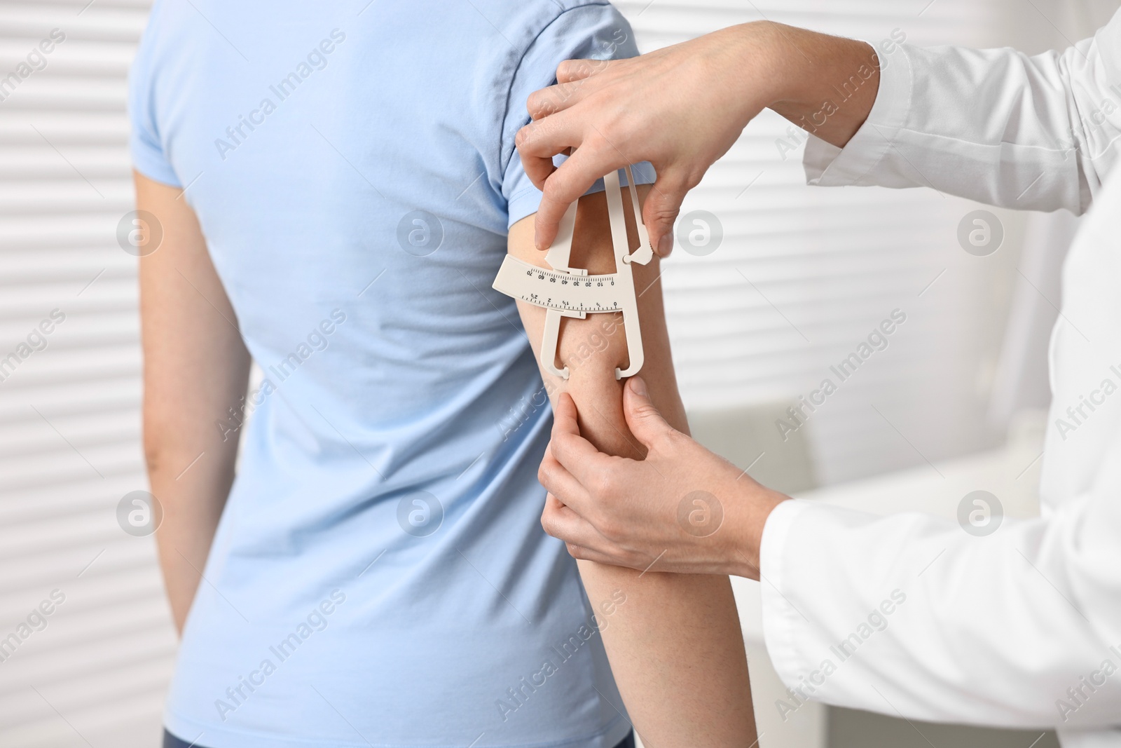 Photo of Doctor measuring woman's body fat with caliper in clinic, closeup