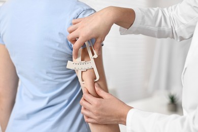 Photo of Doctor measuring woman's body fat with caliper in clinic, closeup