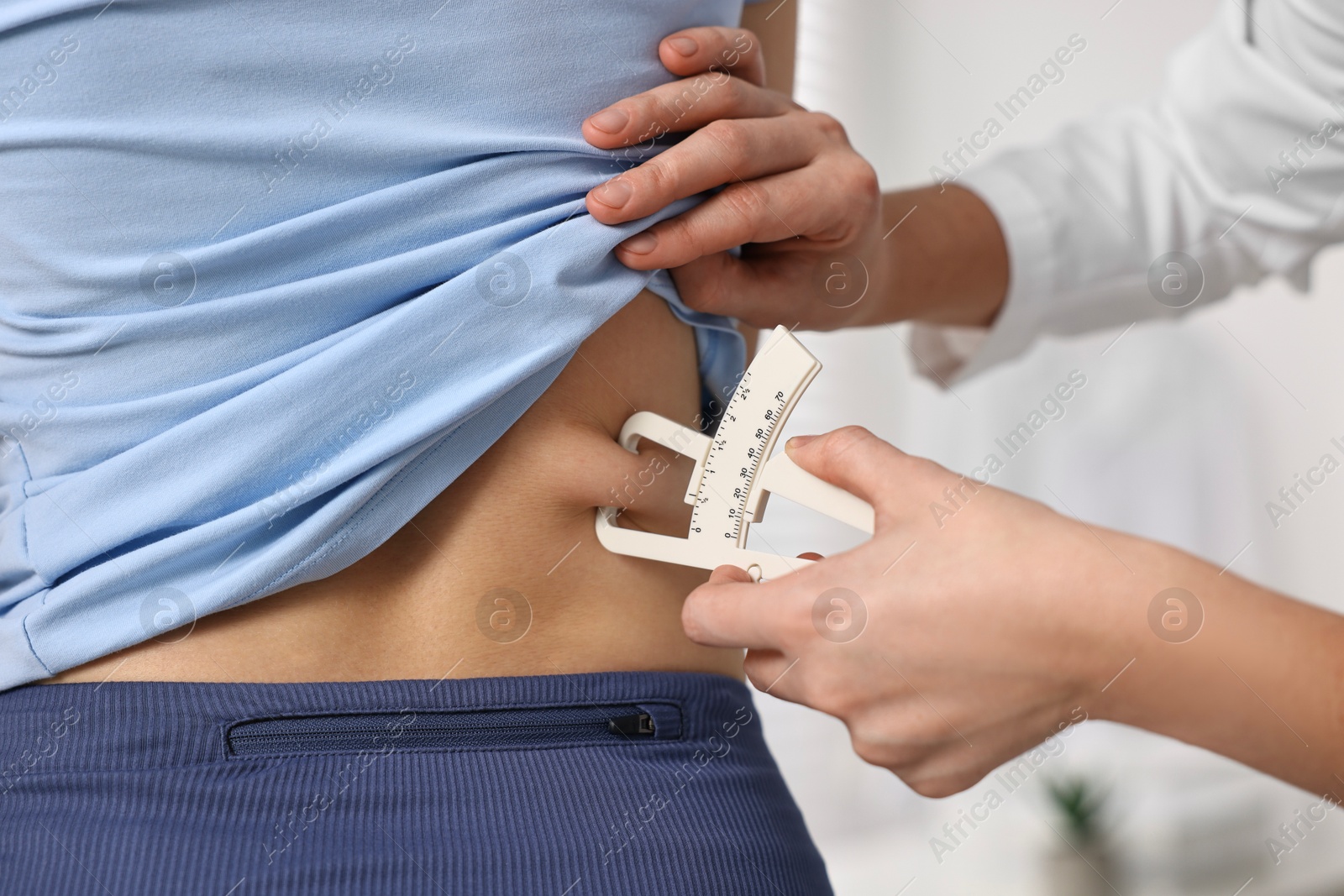 Photo of Doctor measuring woman's body fat with caliper in clinic, closeup