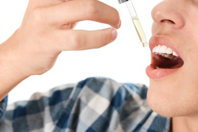 Photo of Young man taking CBD tincture indoors, closeup