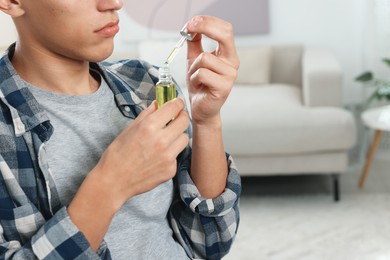 Young man taking CBD tincture indoors, closeup. Space for text