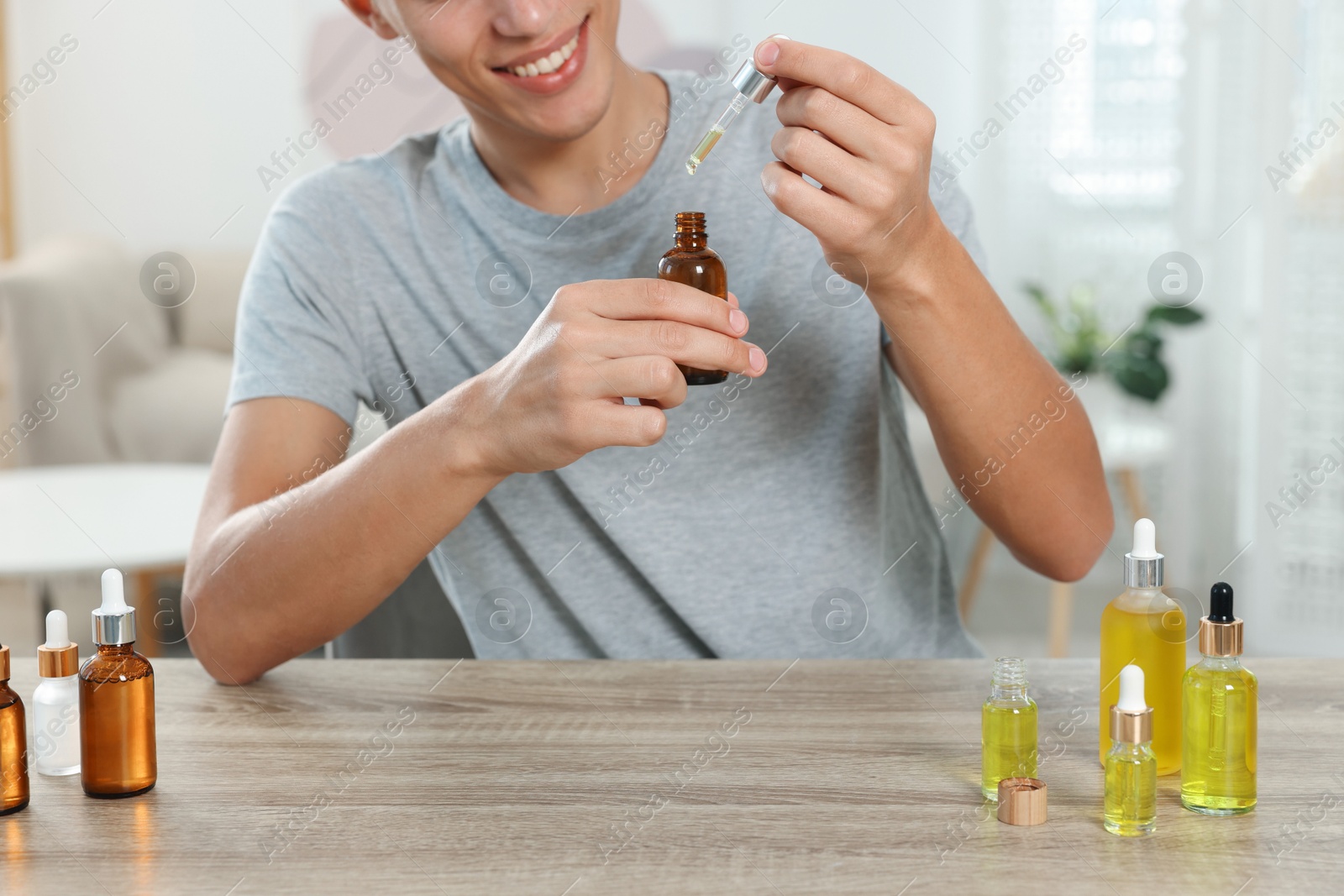 Photo of Young man dripping CBD tincture into bottle from dropper at wooden table, closeup