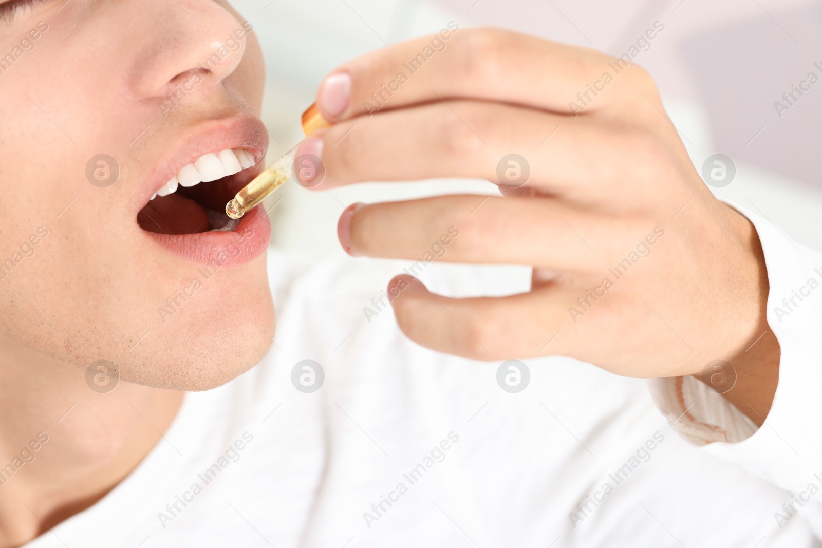 Photo of Young man taking CBD tincture indoors, closeup