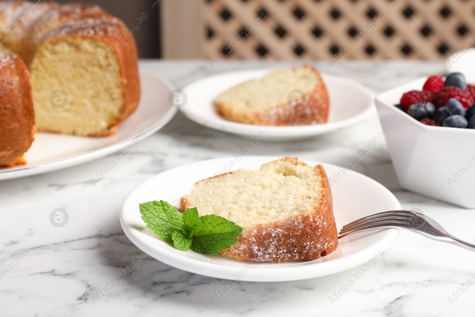 Photo of Freshly baked sponge cake, mint and berries on white marble table, closeup