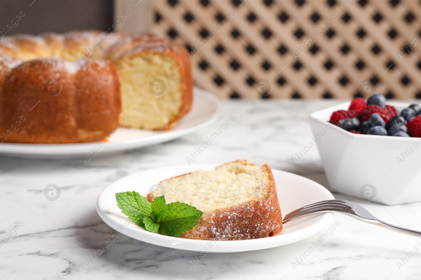 Photo of Freshly baked sponge cake, mint and berries on white marble table, closeup