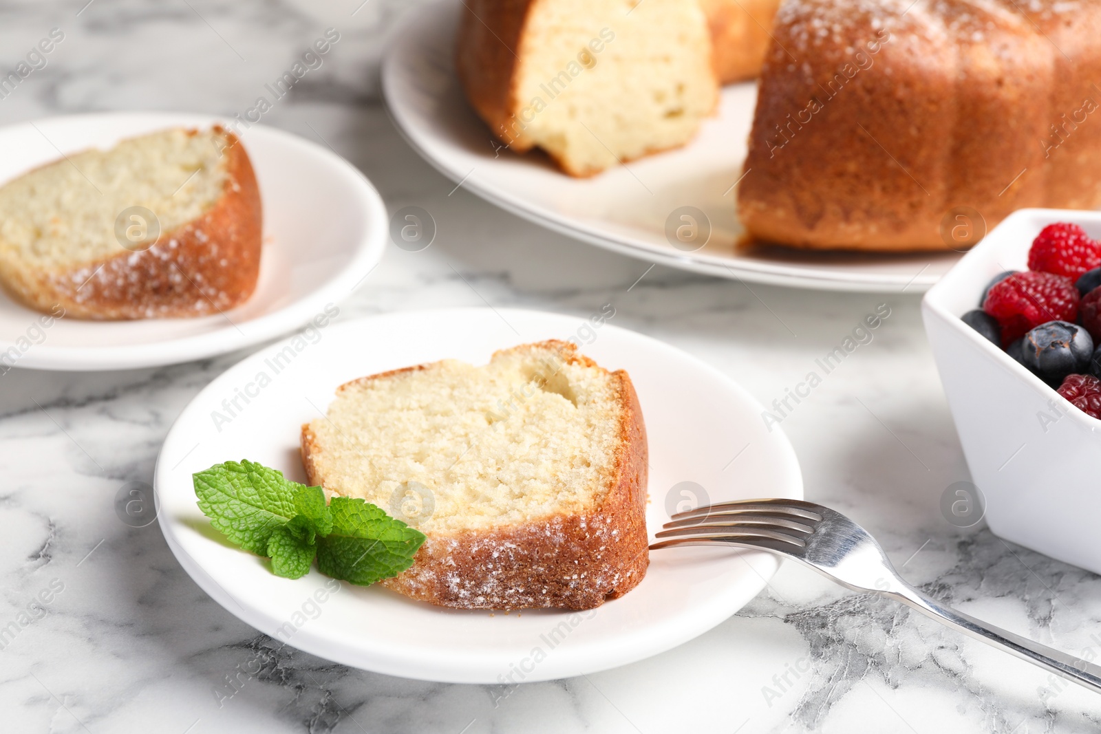 Photo of Freshly baked sponge cake, mint and berries on white marble table, closeup