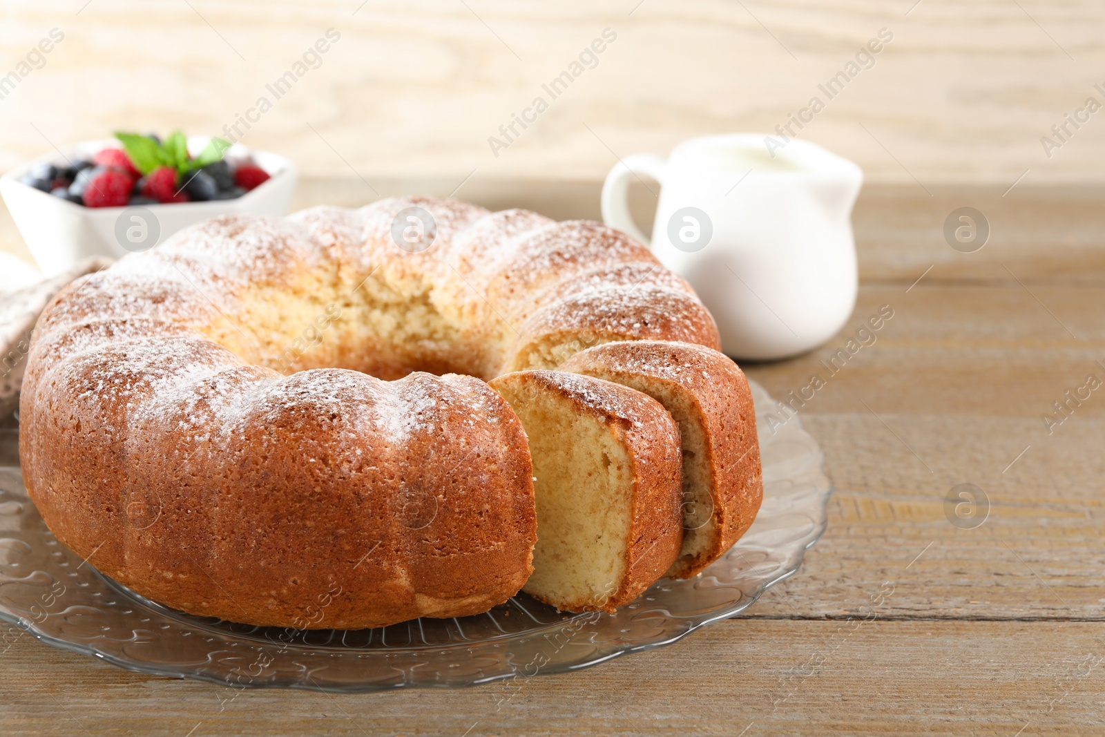 Photo of Freshly baked sponge cake, milk and berries on wooden table, closeup