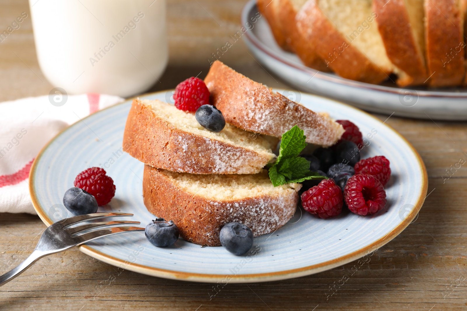 Photo of Pieces of freshly baked sponge cake, berries and milk on wooden table, closeup