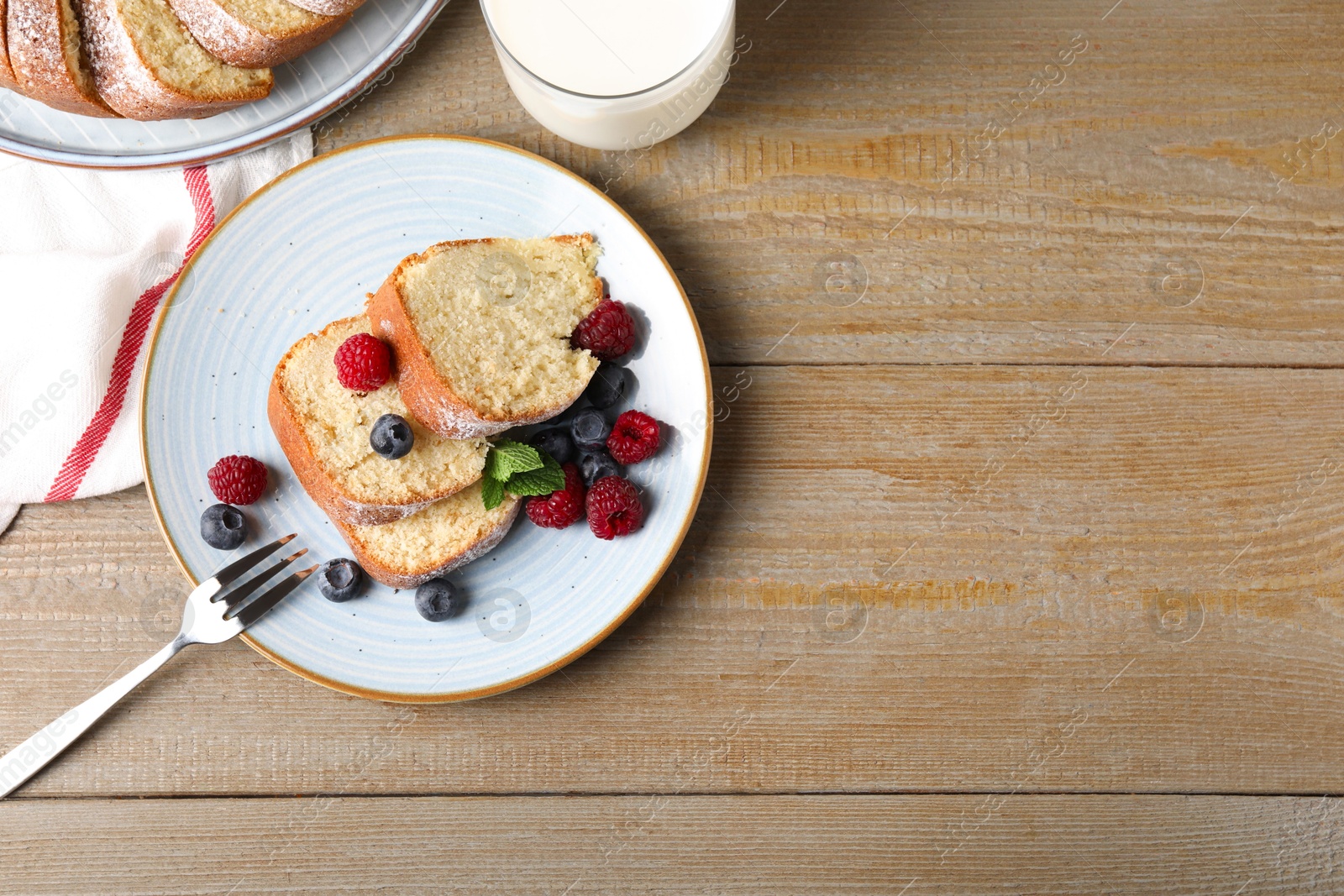 Photo of Pieces of freshly baked sponge cake, berries and milk on wooden table, top view. Space for text