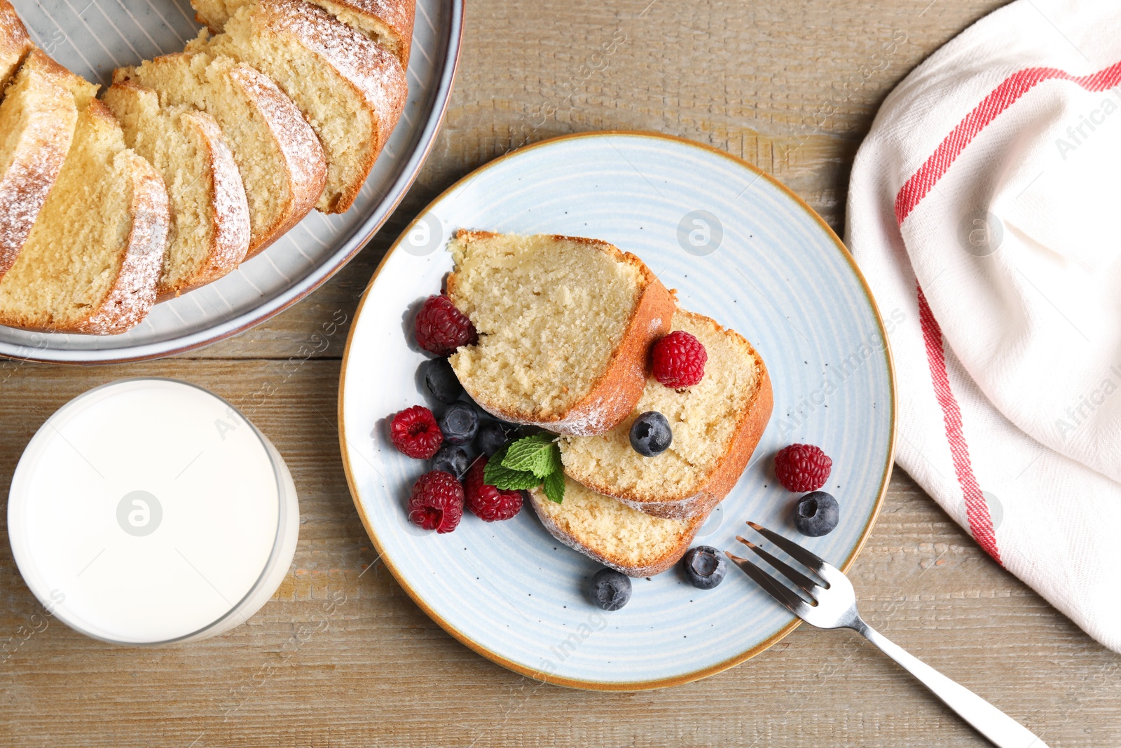 Photo of Pieces of freshly baked sponge cake, berries and milk on wooden table, flat lay