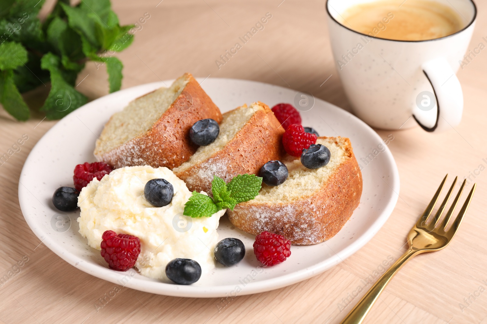 Photo of Pieces of freshly baked sponge cake, berries, ice cream, mint and coffee on wooden table, closeup