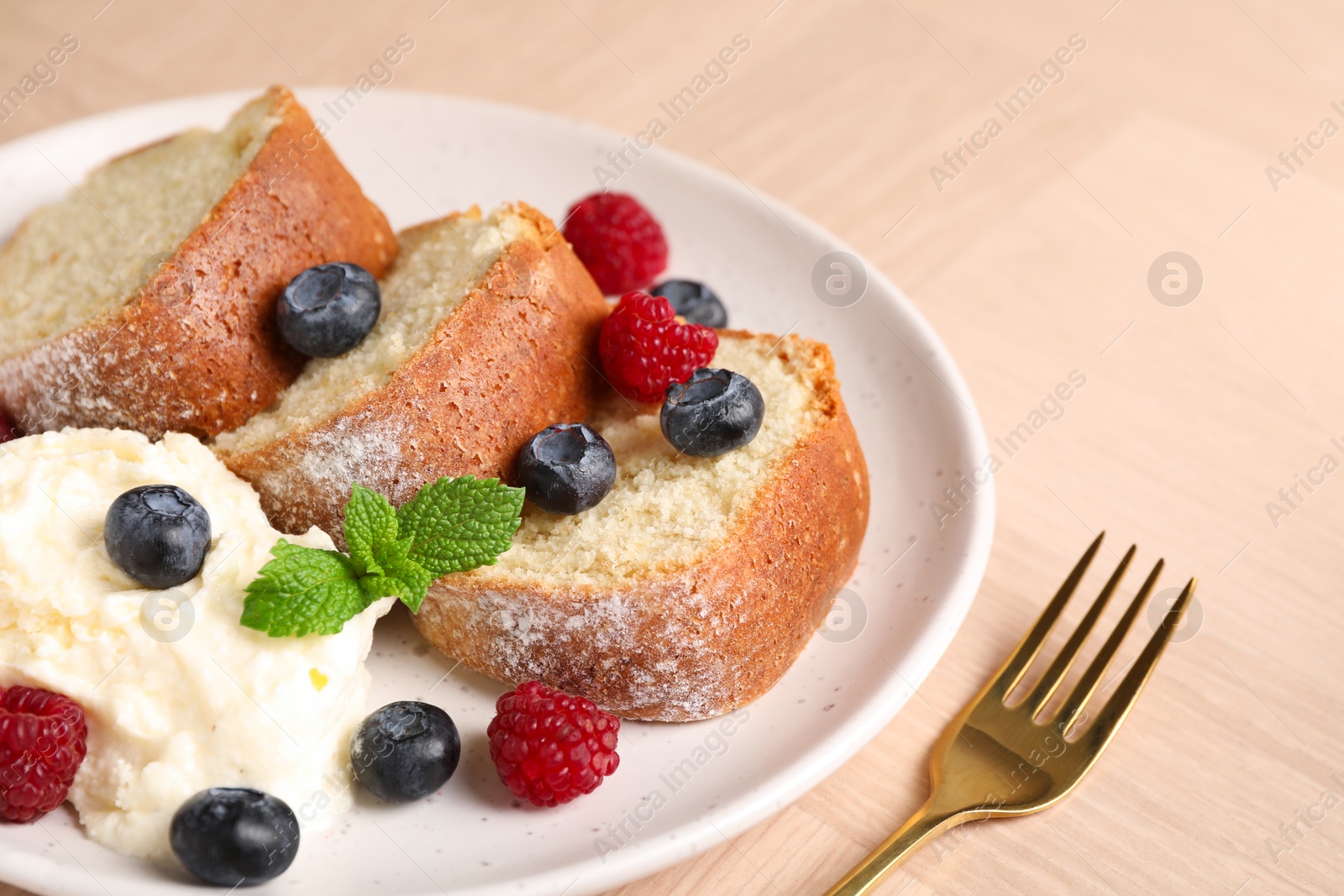 Photo of Pieces of freshly baked sponge cake, berries, ice cream and mint on wooden table, closeup