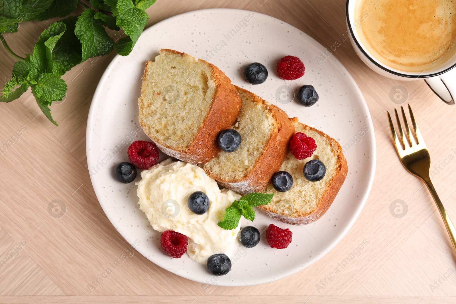 Photo of Pieces of freshly baked sponge cake, berries, ice cream, mint and coffee on wooden table, flat lay