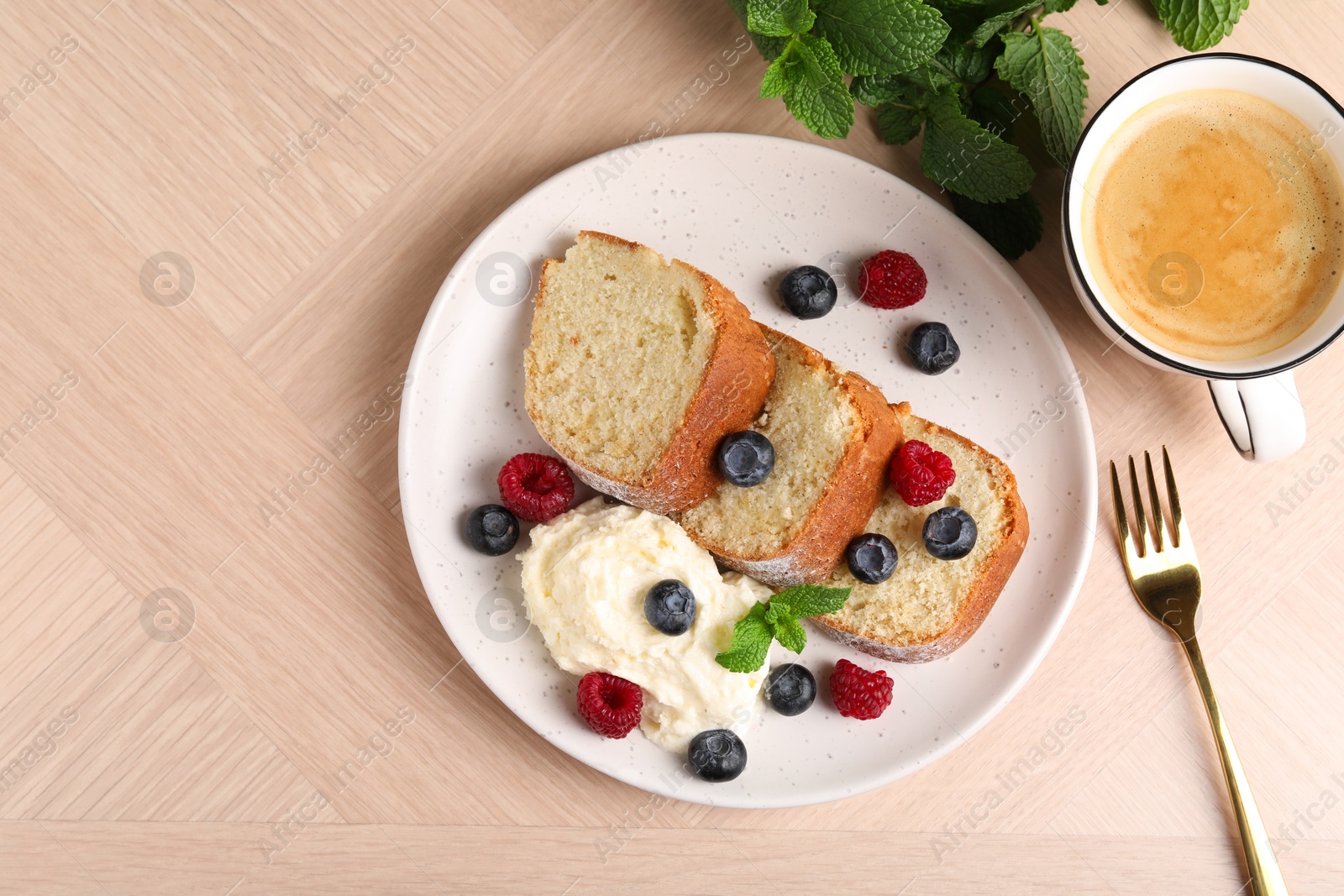 Photo of Pieces of freshly baked sponge cake, berries, ice cream, mint and coffee on wooden table, flat lay