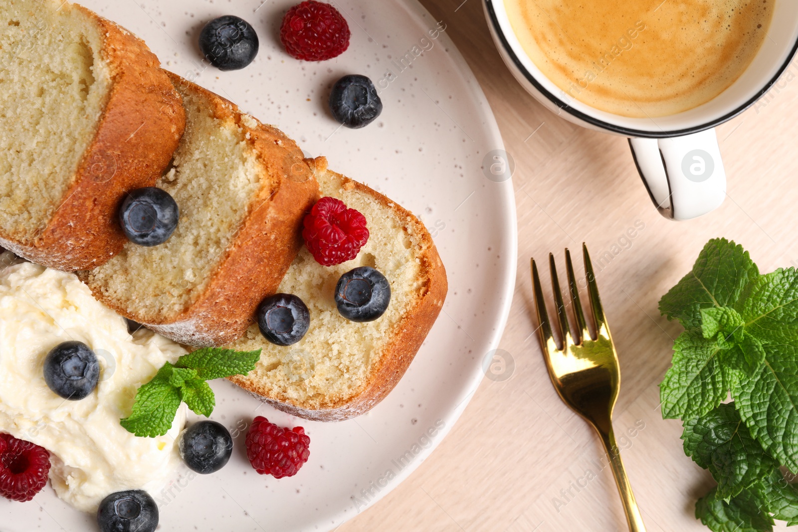 Photo of Pieces of freshly baked sponge cake, berries, ice cream, mint and coffee on wooden table, flat lay