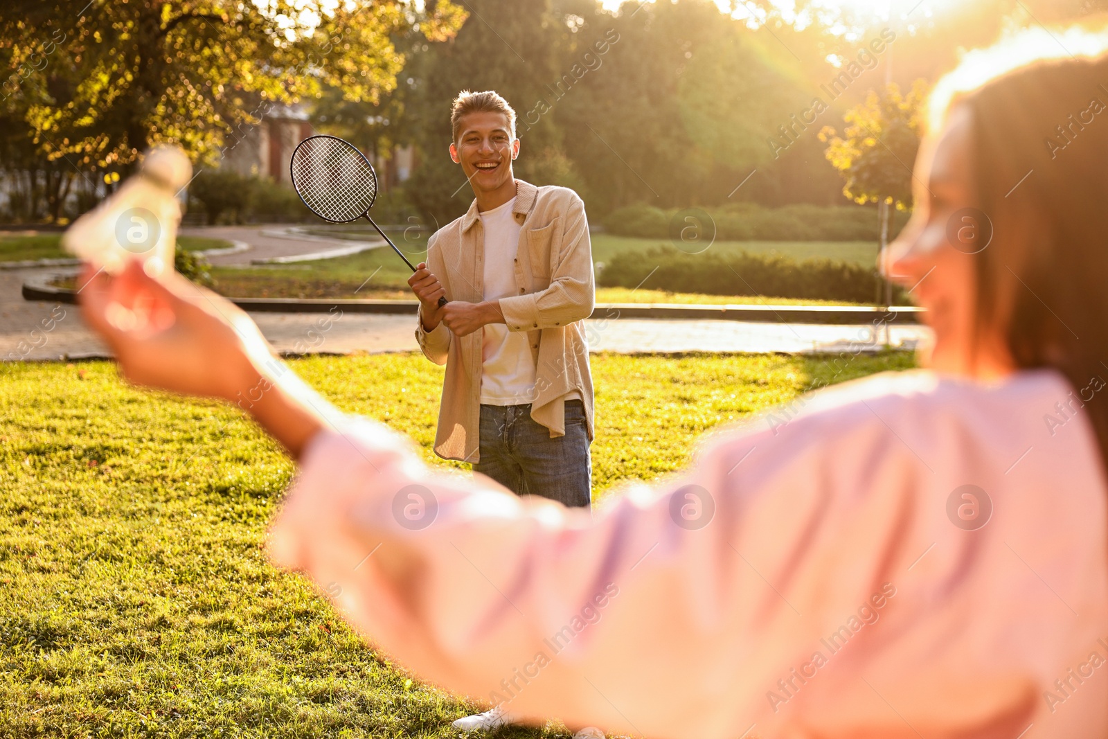 Photo of Young woman and man playing badminton in park on sunny day, selective focus