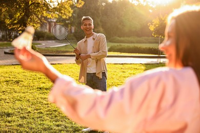 Photo of Young woman and man playing badminton in park on sunny day, selective focus