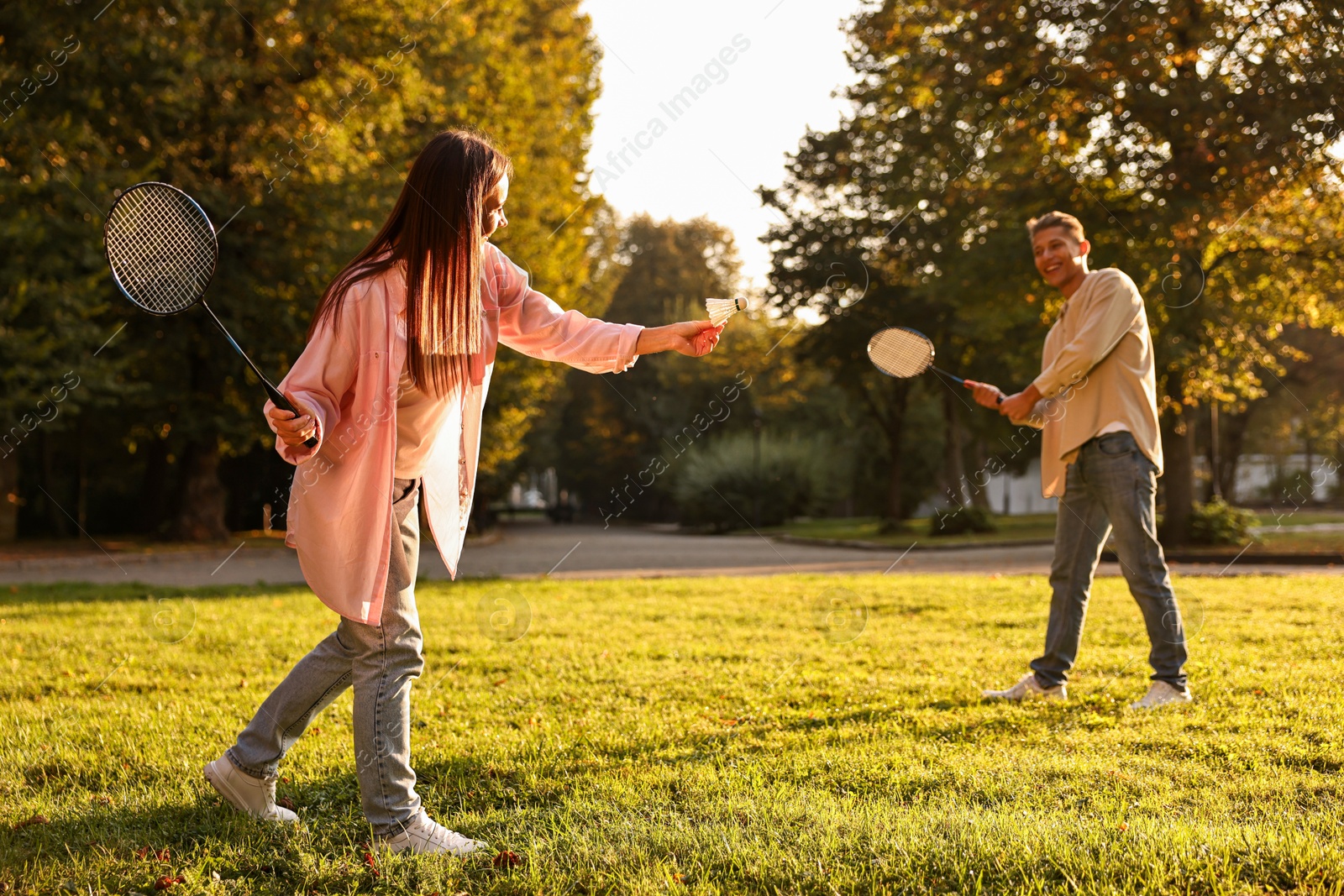 Photo of Young woman and man playing badminton in park on sunny day, selective focus