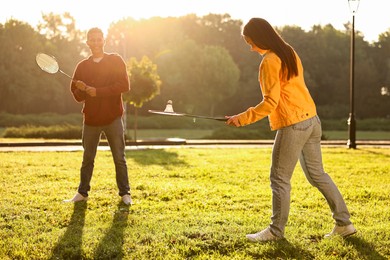 Photo of Young man and woman playing badminton in park on sunny day, selective focus