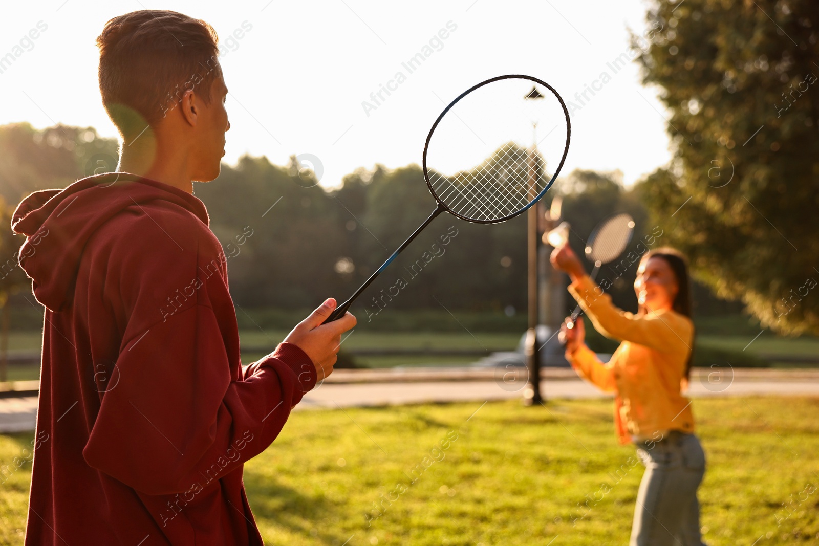 Photo of Young man and woman playing badminton in park on sunny day, selective focus