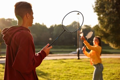 Photo of Young man and woman playing badminton in park on sunny day, selective focus