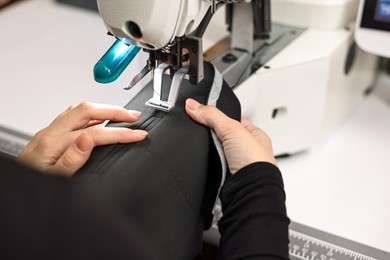 Photo of Woman working with sewing machine at white table in professional workshop, closeup