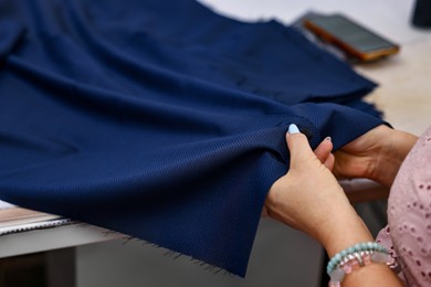 Photo of Woman sewing fabric at table in professional workshop, closeup