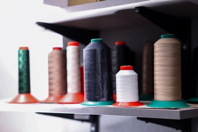 Photo of Many different spools of thread on white shelf in professional workshop