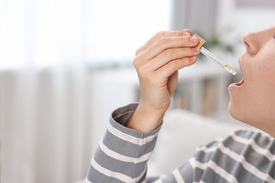 Photo of Young woman taking CBD tincture indoors, closeup. Space for text