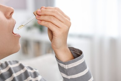 Photo of Young woman taking CBD tincture indoors, closeup